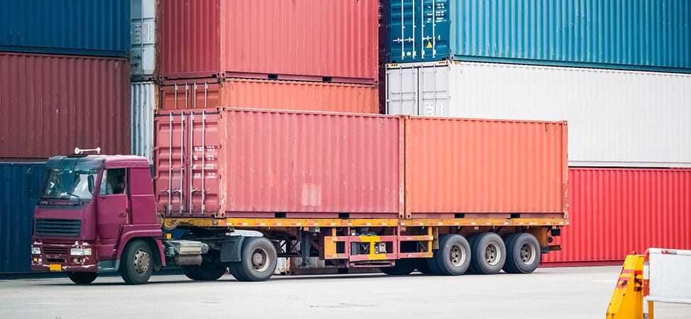 Truck transporting stacked shipping containers at port.